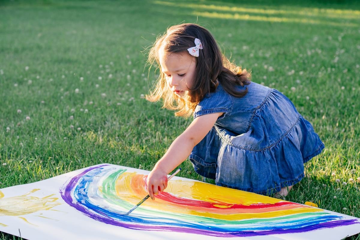 Una bambina dipinge un grande arcobaleno su un foglio, sul prato