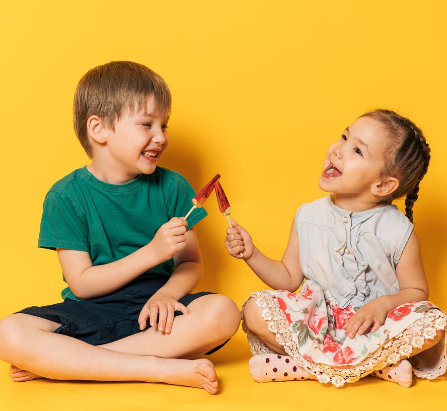Due bambini seduti a gambe incrociate ridono insieme con un ghiacciolo in mano